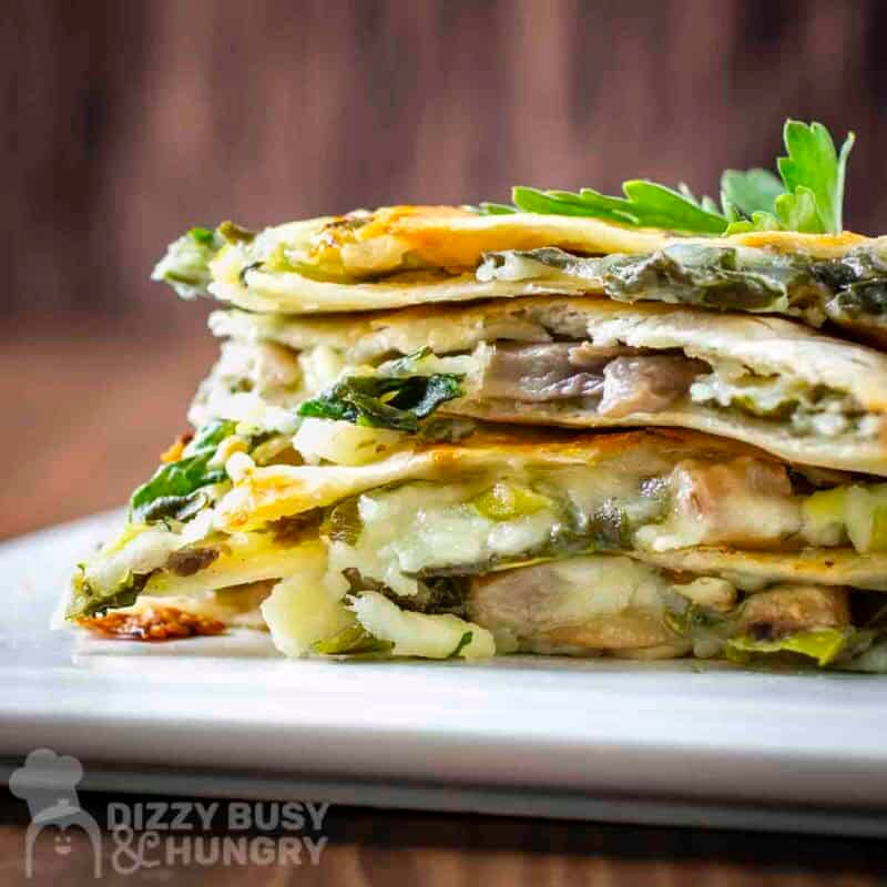 Side shot of multiple slices of spinach mushroom quesadillas stacked on a white plate garnished with fresh parsley.