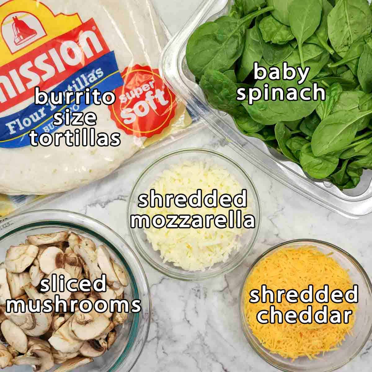 Overhead view of ingredients - burrito size tortillas, baby spinach, shredded mozzarella, sliced mushrooms, and shredded cheddar.