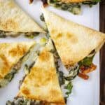 Overhead close up shot of multiple slices of spinach mushroom quesadillas on a white plate.
