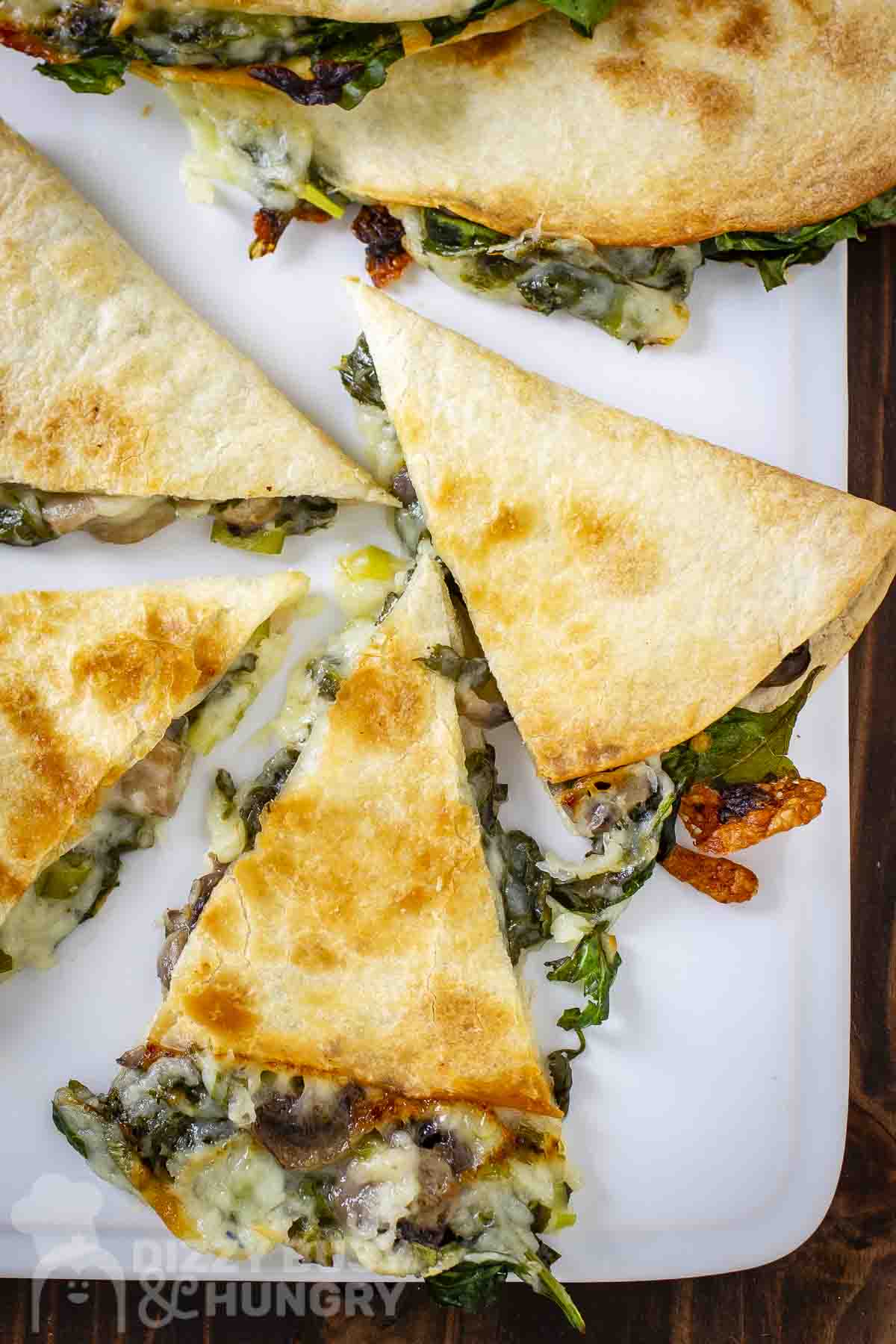 Overhead close up shot of multiple slices of spinach mushroom quesadillas on a white plate.