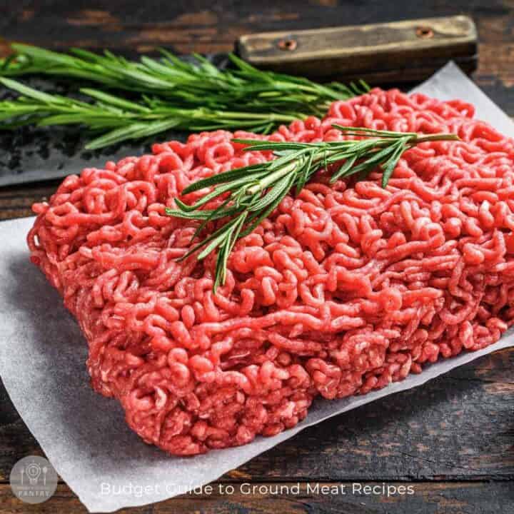 Ground beef, fresh rosemary, and sage on parchment paper sitting on a dark butcher's block counter for delicious ground meat recipes.