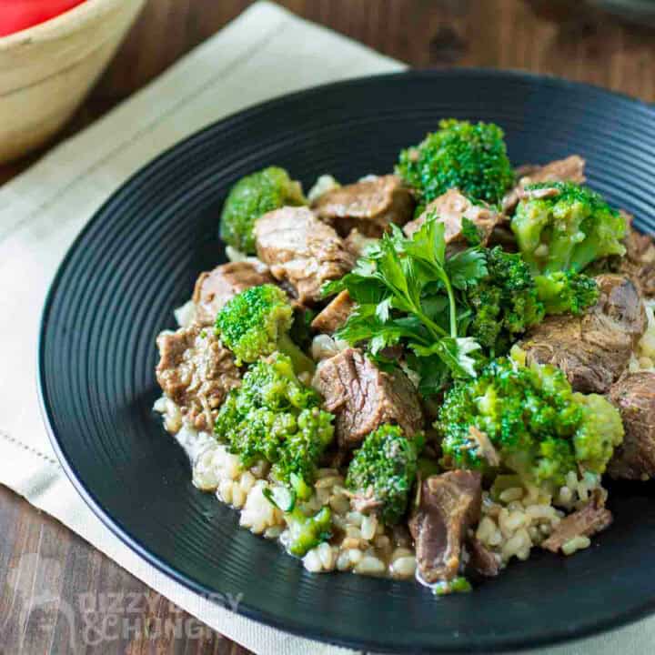 Side shot of beef and broccoli on a bed of rice garnished with fresh parsley on a black plate.