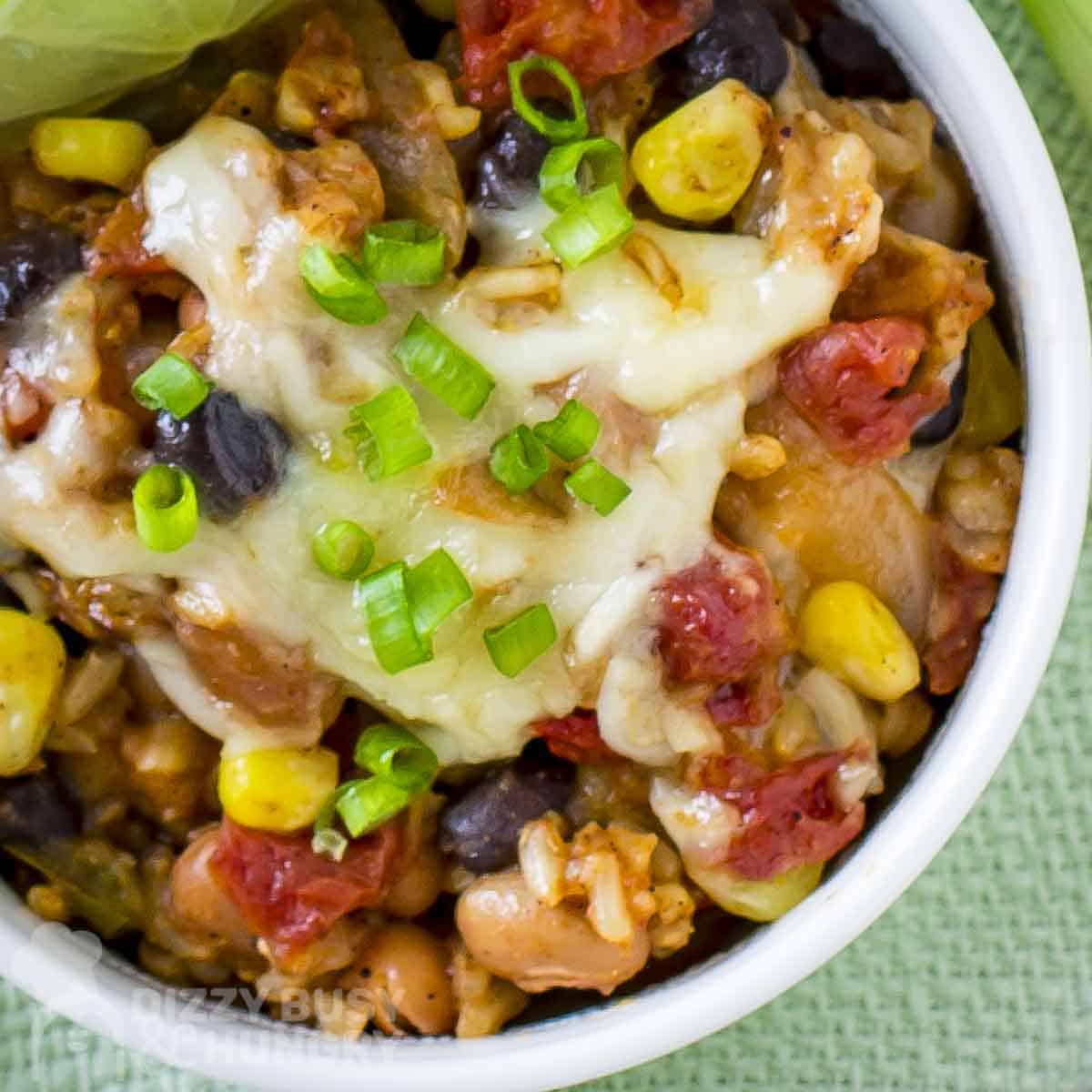 Overhead close up shot of enchilada bake garnished with chopped green onions in a white bowl on a green placemat.