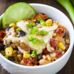 Close up shot of enchilada bake garnished with chopped green onions and a lime wedge in a white bowl on a green placemat.