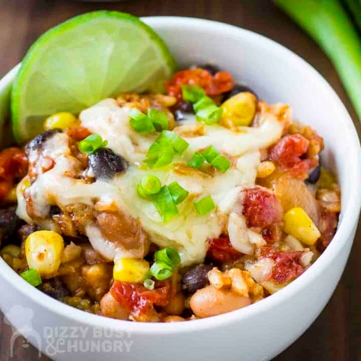 Close up shot of enchilada bake garnished with chopped green onions and a lime wedge in a white bowl on a green placemat.