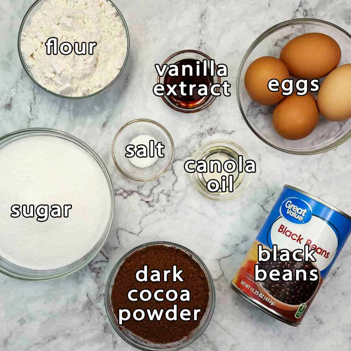 Overhead shot of ingredients - flour, sugar, dark cocoa powder, black beans, eggs, vanilla extract, salt, and canola oil.
