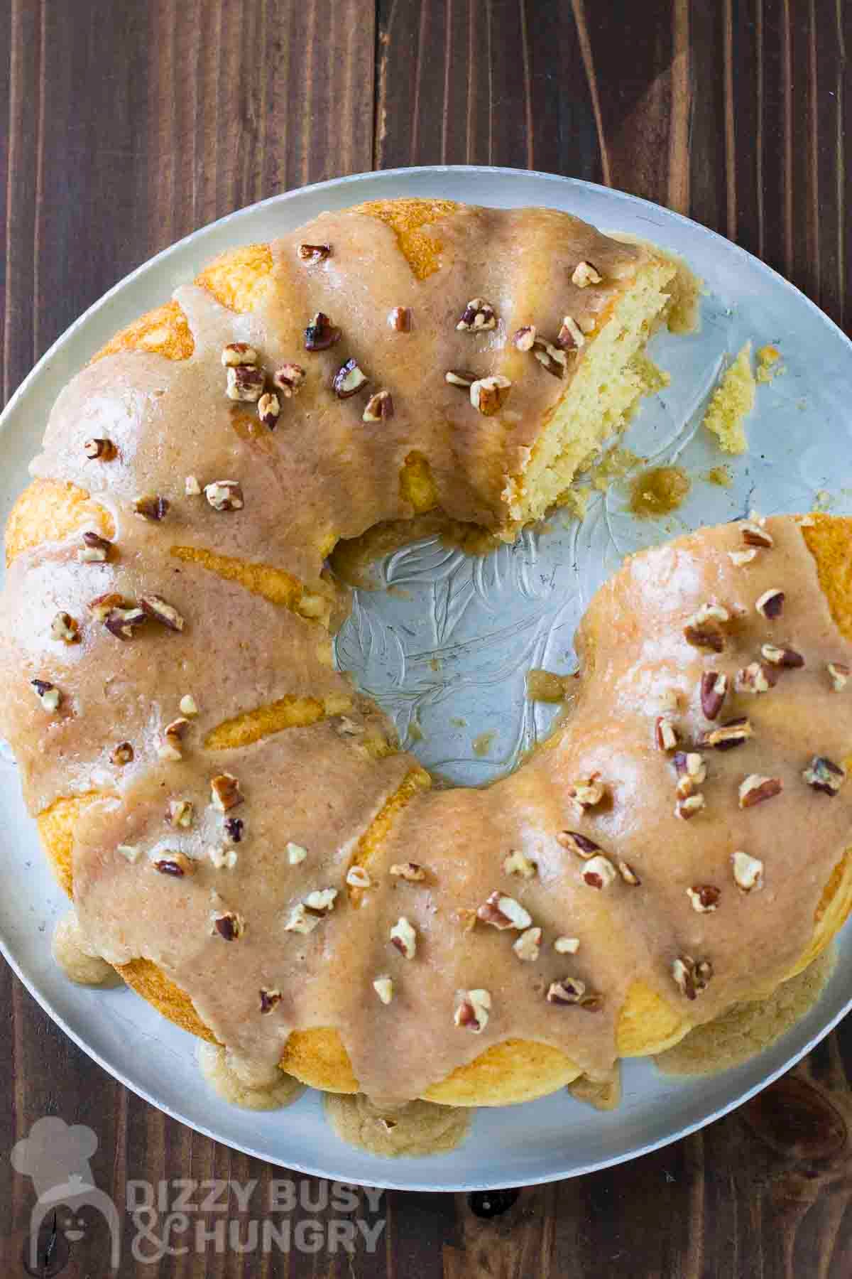 Overhead shot of bundt cake with a piece taken out on a silver serving tray on a wooden table.