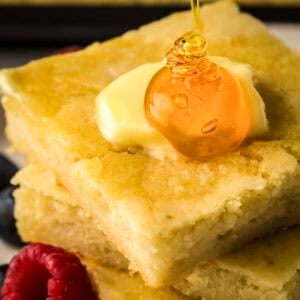 Side close up shot of two pancakes stacked on each other with a pad of butter and drizzle of maple syrup on top.