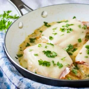 Close up shot of two pieces of chicken cordon bleu garnished with fresh parsley in a skillet all on a blue and white cloth.