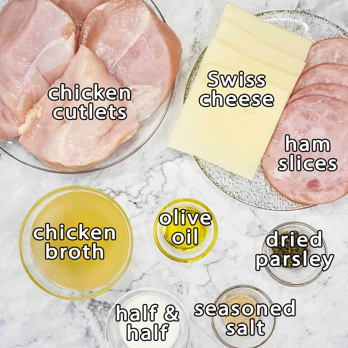 Overhead shot of ingredients - chicken cutlets, swiss cheese, ham slices, chicken broth, olive oil, dried parsley, seasoned salt, and half & half.