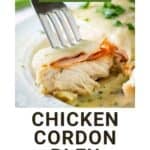 Side close up shot of a fork holding a piece of chicken cordon bleu on a white plate.