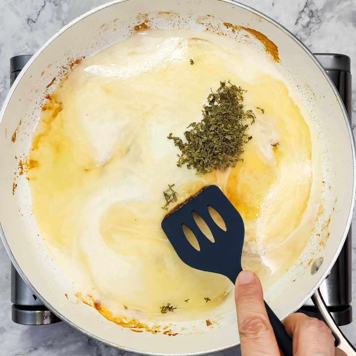 Overhead view of someone scraping a pan with a spatula to deglaze to show how pan sauce secrets can elevate your dinner. 