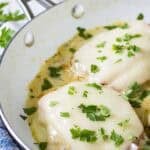 Close up shot of two pieces of chicken cordon bleu garnished with fresh parsley in a skillet all on a blue and white cloth.