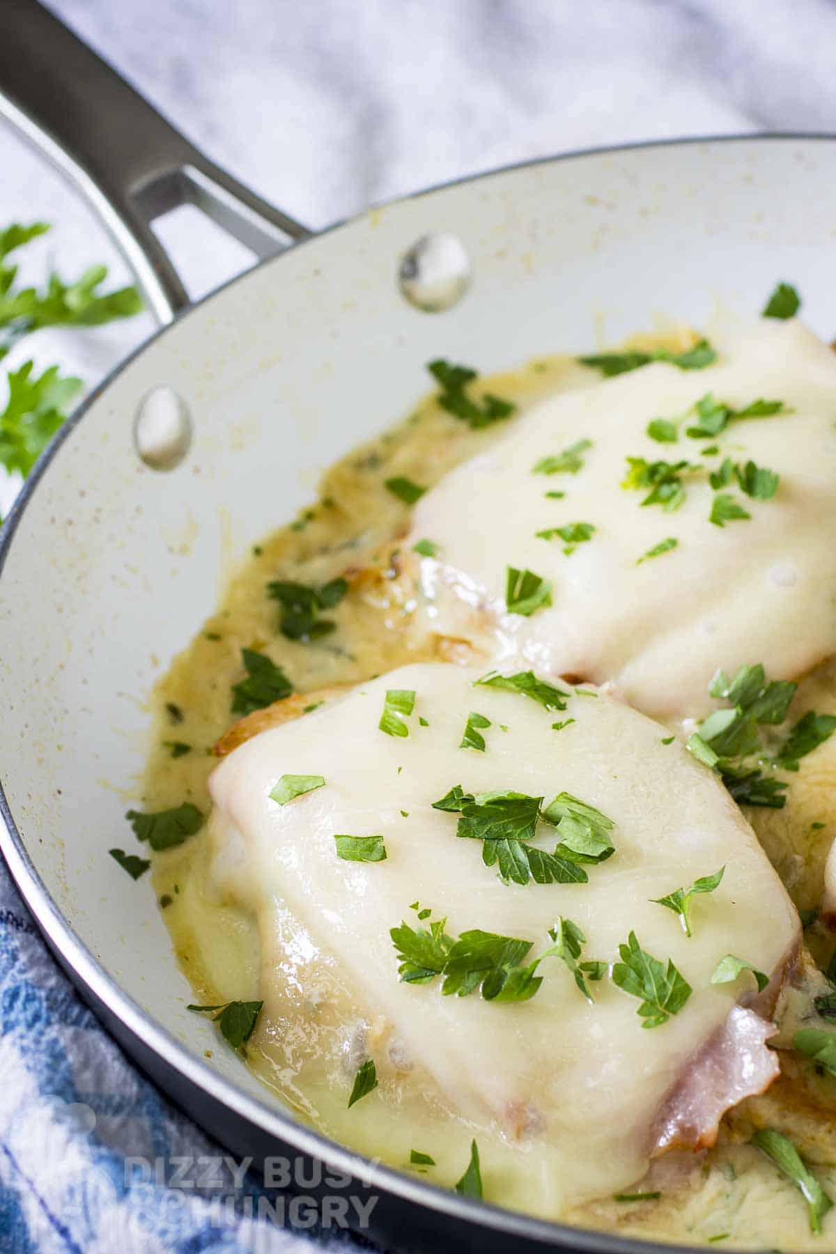 Close up shot of two pieces of chicken cordon bleu garnished with fresh parsley in a skillet all on a blue and white cloth.