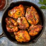 Overhead shot of BBQ chicken thighs in a cast iron skillet garnished with fresh parsley.