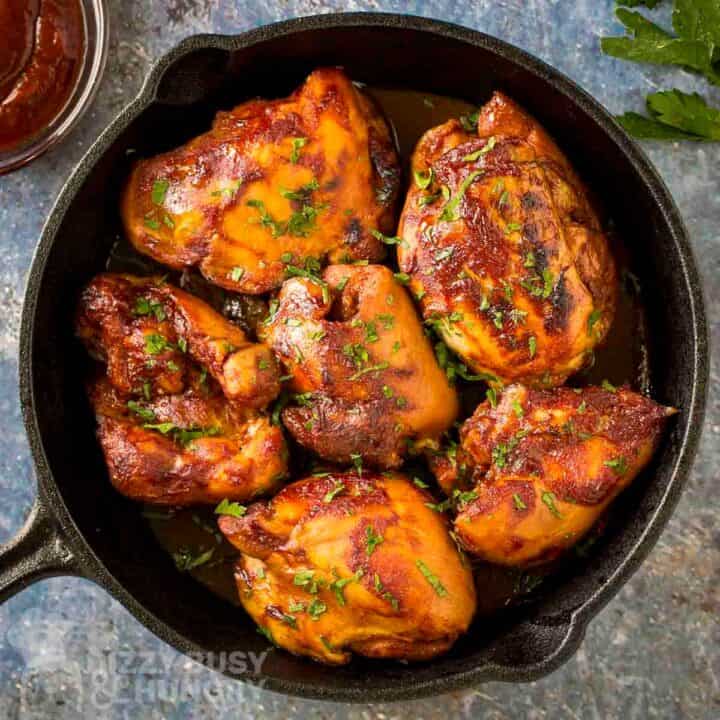 Overhead shot of BBQ chicken thighs in a cast iron skillet garnished with fresh parsley.
