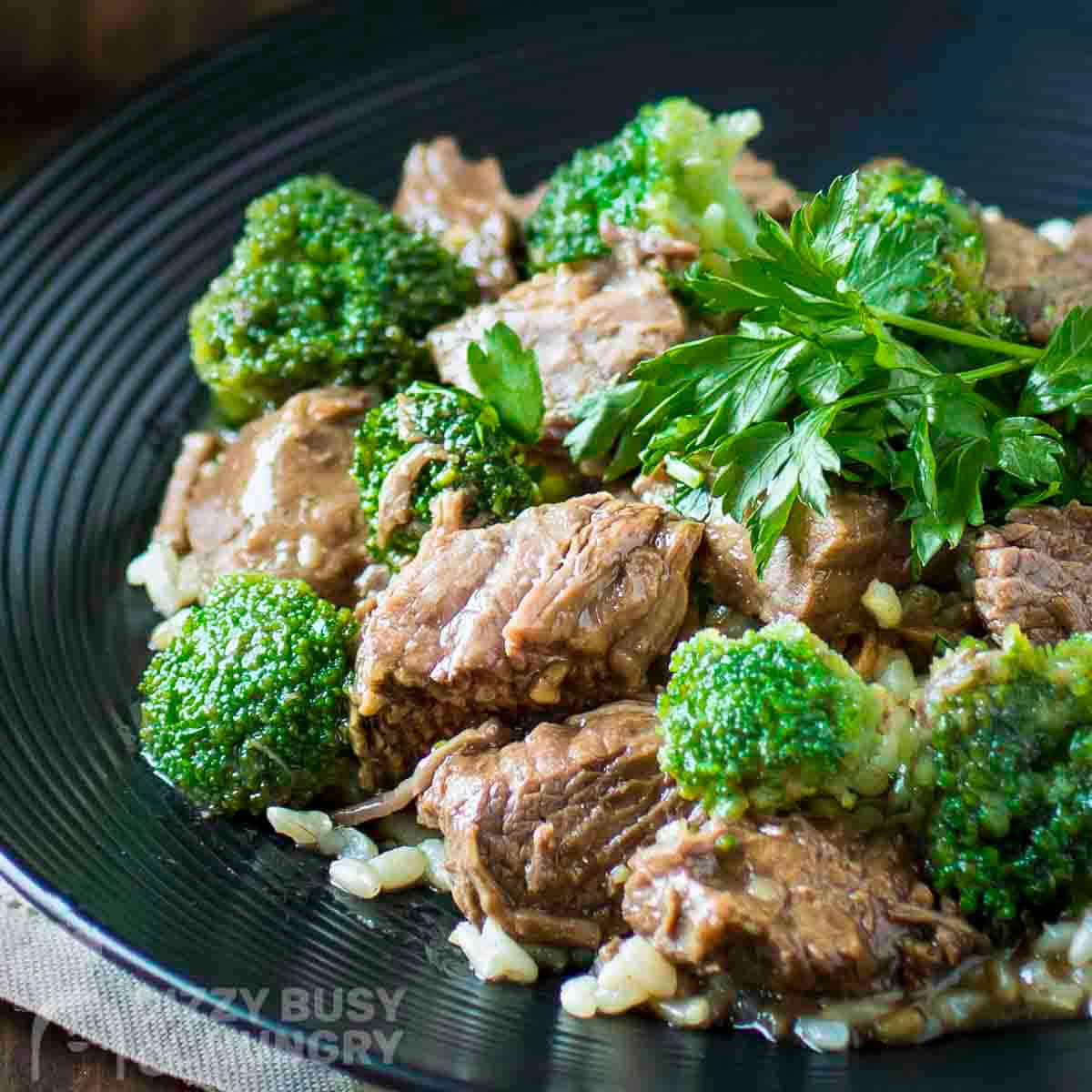 Side shot of beef and broccoli on a bed of rice garnished with fresh parsley on a black plate.