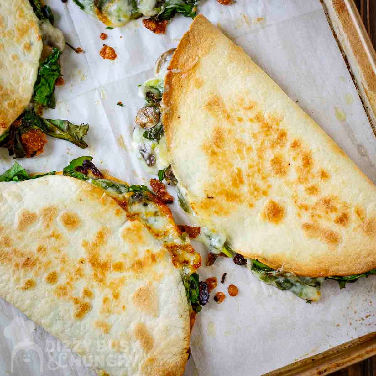 Overhead view of whole spinach mushroom quesadillas on a baking sheet lined with parchment paper.