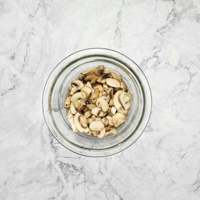 Overhead view of process shot 1 - place the mushrooms in a microwave safe bowl and microwave for 2 minutes to soften them. Drain the mushrooms and set aside.