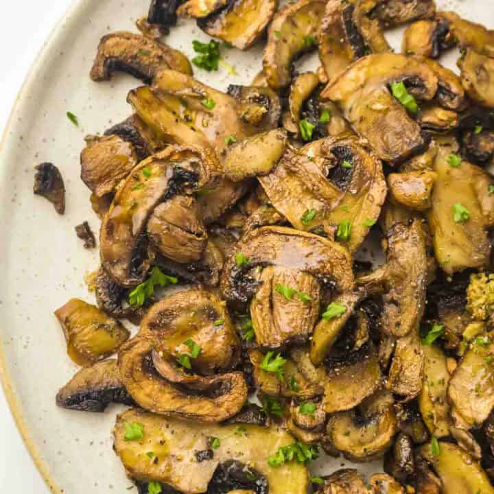Overhead close up shot of air fryer mushrooms garnished with fresh parsley on a speckled white plate.