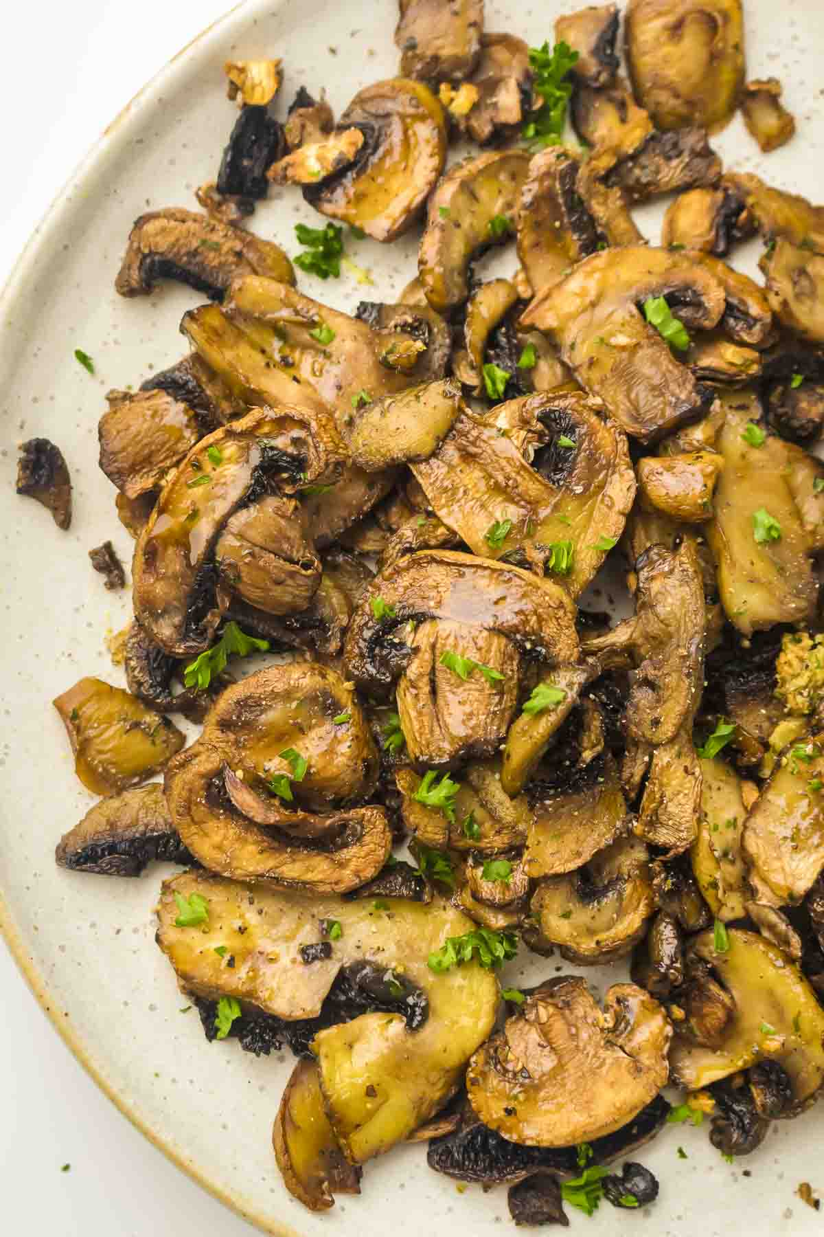 Overhead close up shot of air fryer mushrooms garnished with fresh parsley on a speckled white plate.
