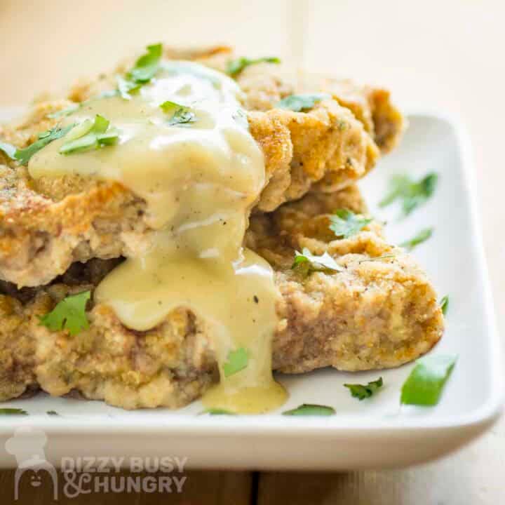 Side shot of chicken fried steak with gravy and fresh parsley on top on a white plate.