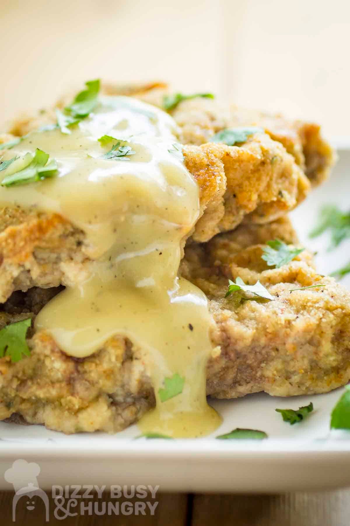 Side shot of chicken fried steak with gravy and fresh parsley on top on a white plate.
