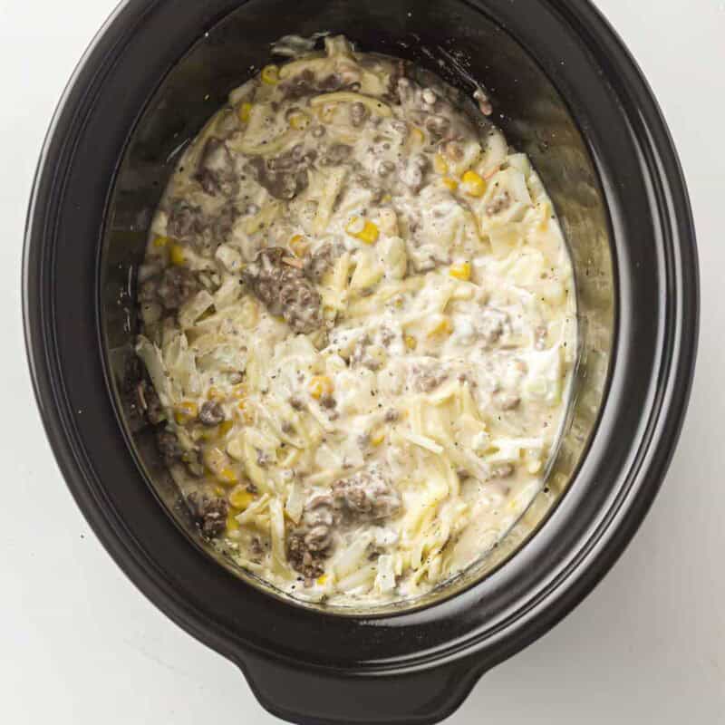 Overhead view of process shot 1 - add the browned grounded beef, corn, soup, sour cream, cheese, onion, garlic powder, salt & pepper, then stir to combine.