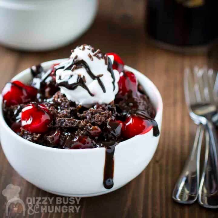 Side view of Guinness chocolate cake in a white bowl with forks and a glass in the background.