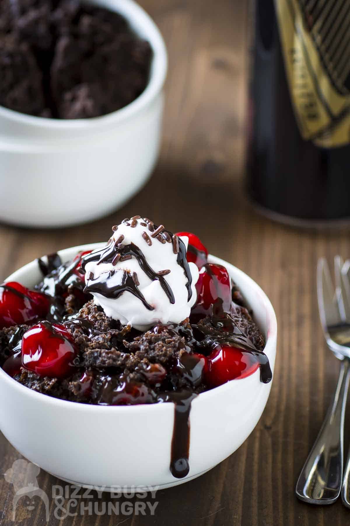 Side view of Guinness chocolate cake in a white bowl with forks and a glass in the background.