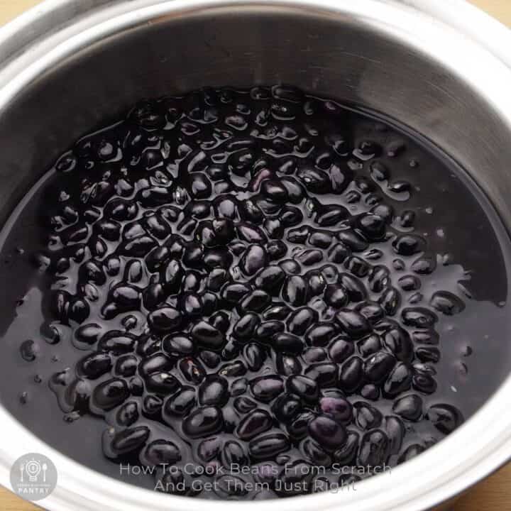 A large pot filled with water and black beans, with text overlay How To Cook Beans From Scratch.
