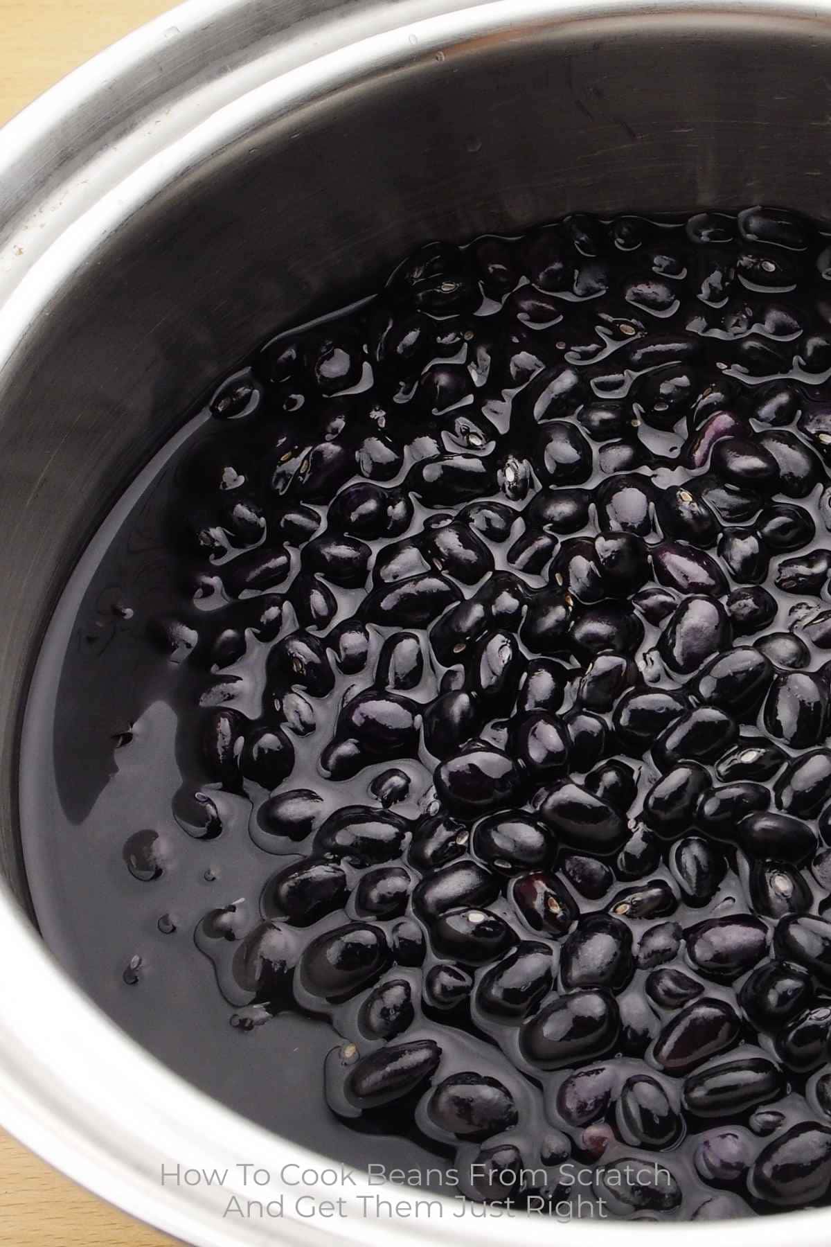 Black beans in water in a large pot with text overlay How To Cook Beans From Scratch.