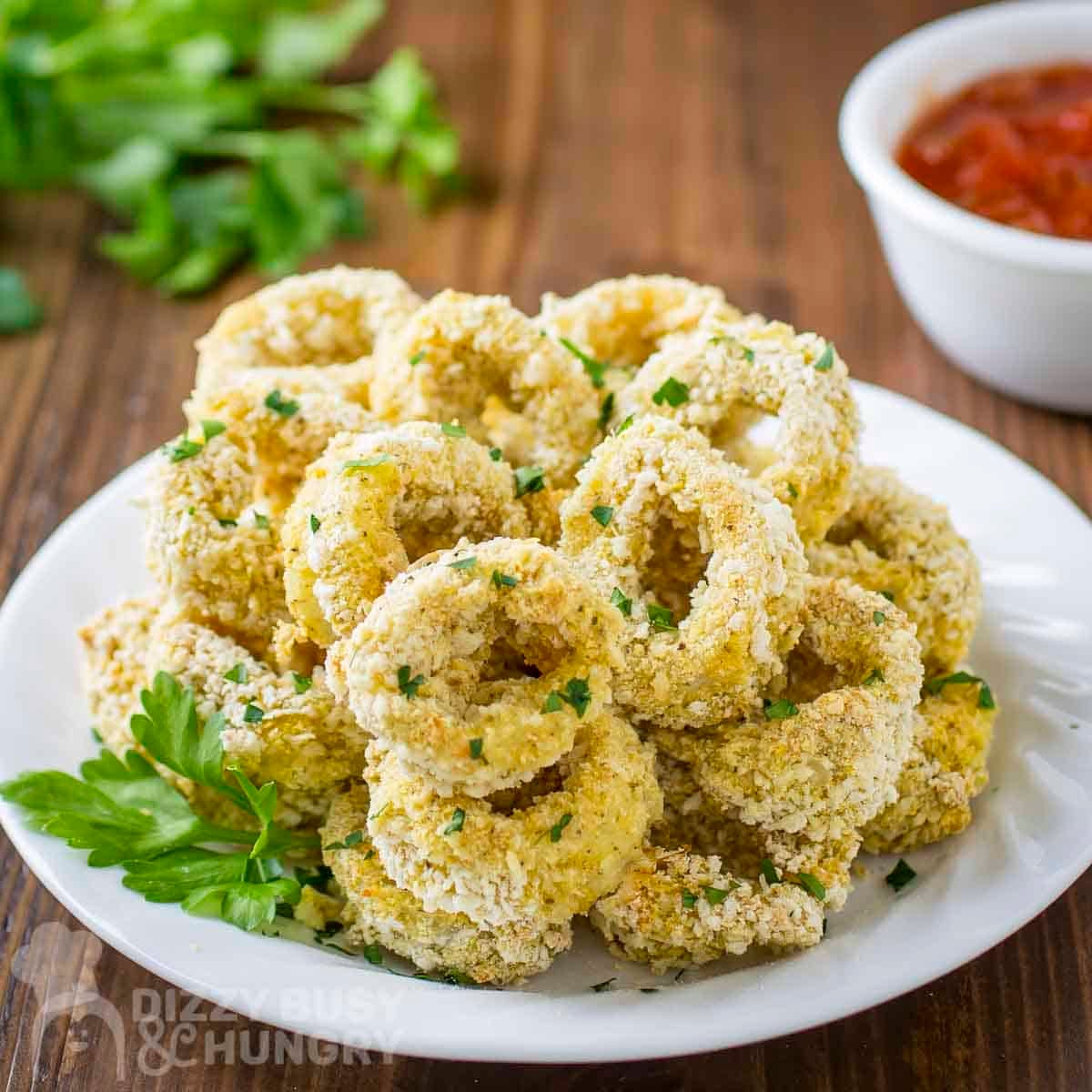 Side view of baked calamari with herbs on a white plate.