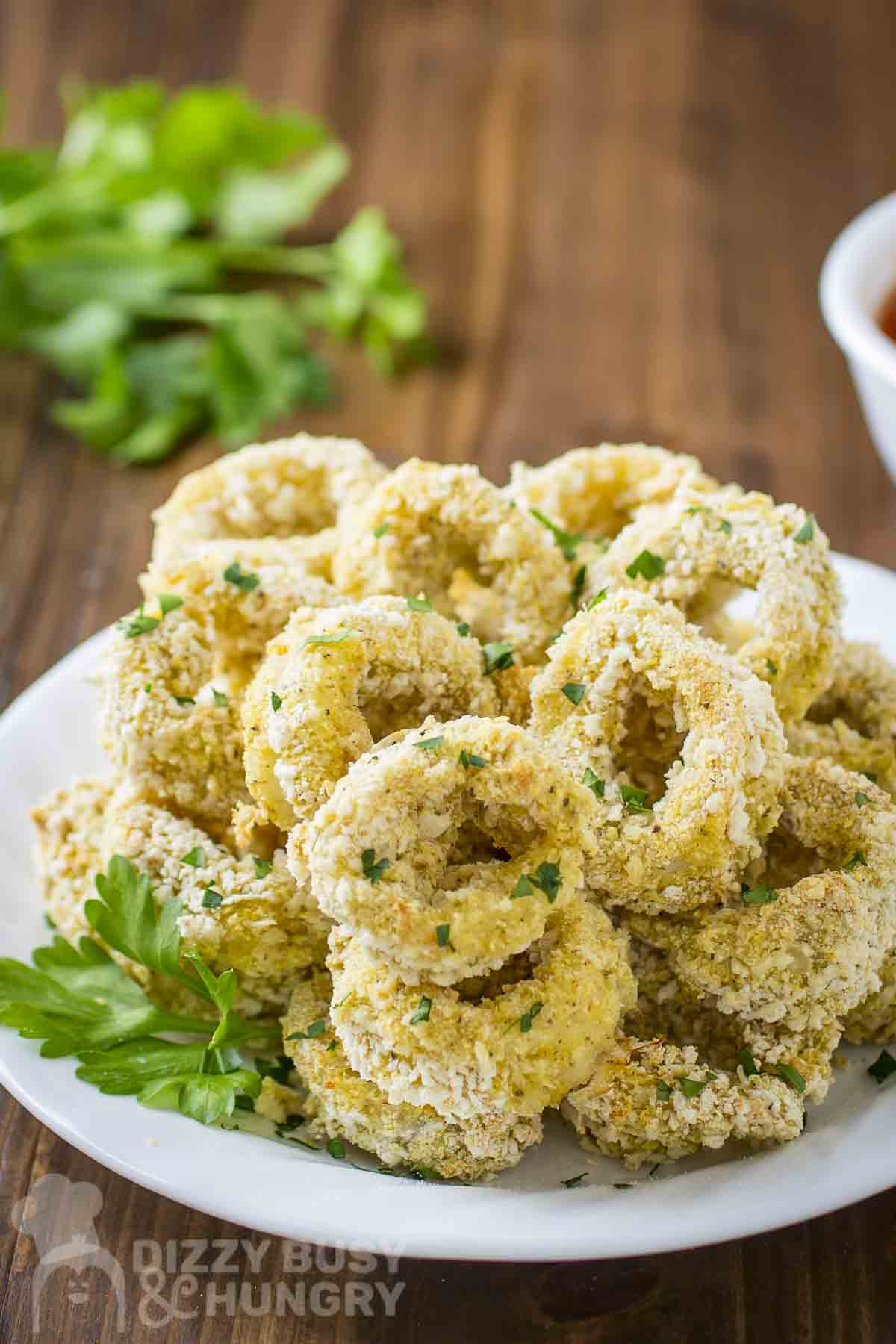 Side view of baked calamari with herbs on a white plate.