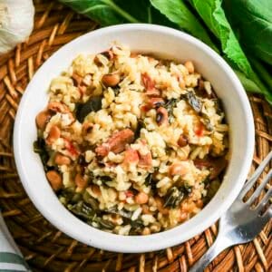 Close up overhead shot of black eyed peas and collard greens in a white bowl with fresh collard greens and a fork on the side.