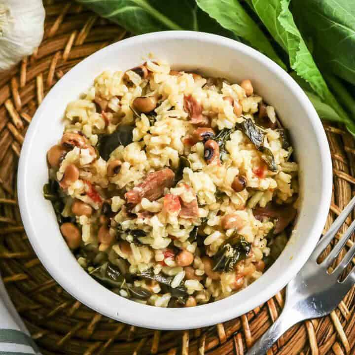 Close up overhead shot of black eyed peas and collard greens in a white bowl with fresh collard greens and a fork on the side.