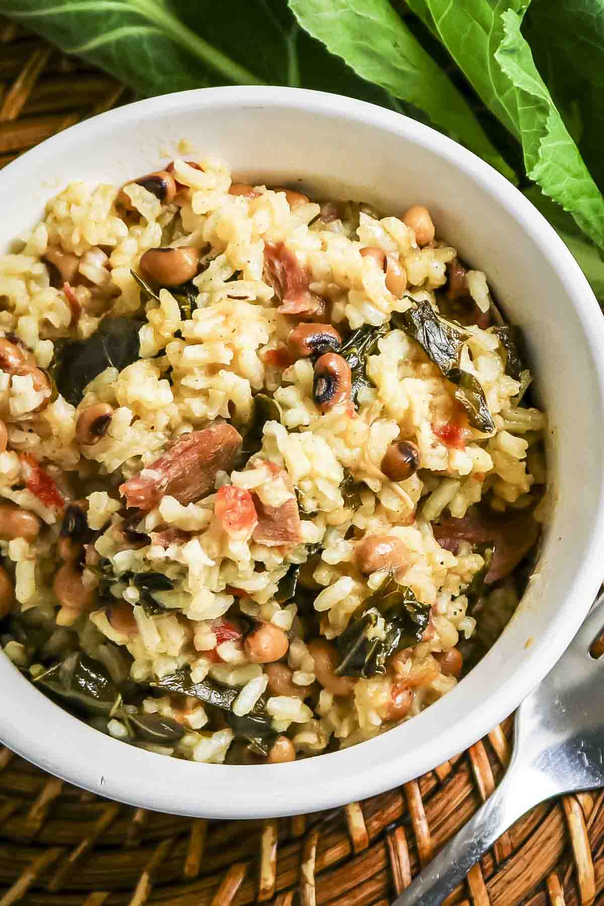 Close up overhead shot of black eyed peas and collard greens in a white bowl with fresh collard greens and a fork on the side.
