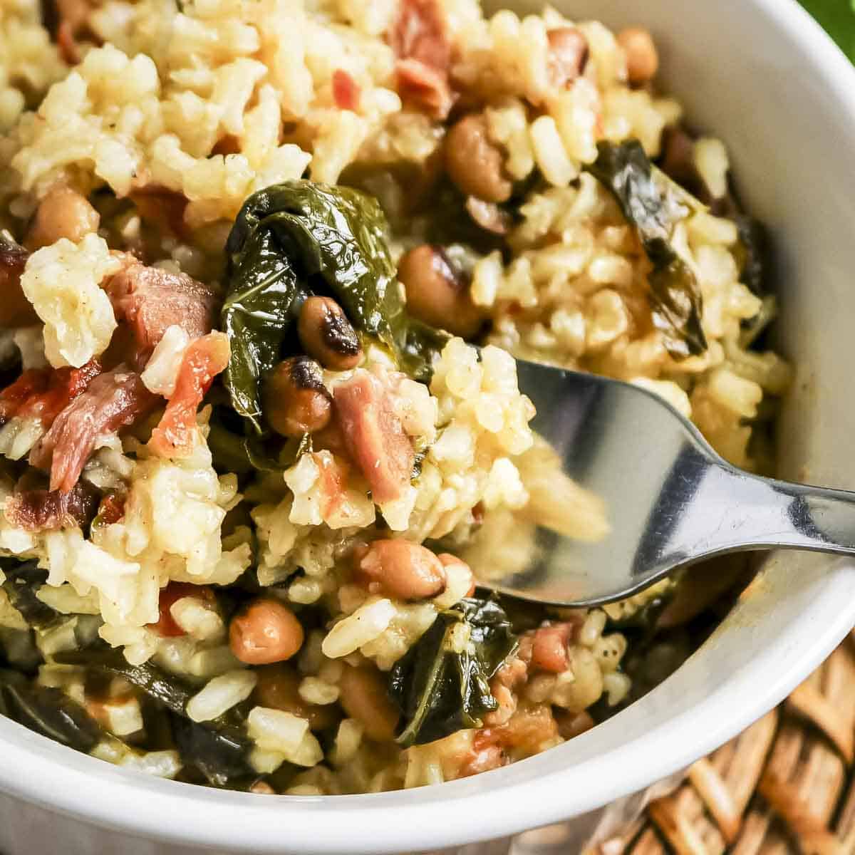 Close up shot of a fork scooping black eyed peas and collard greens out of a white bowl.
