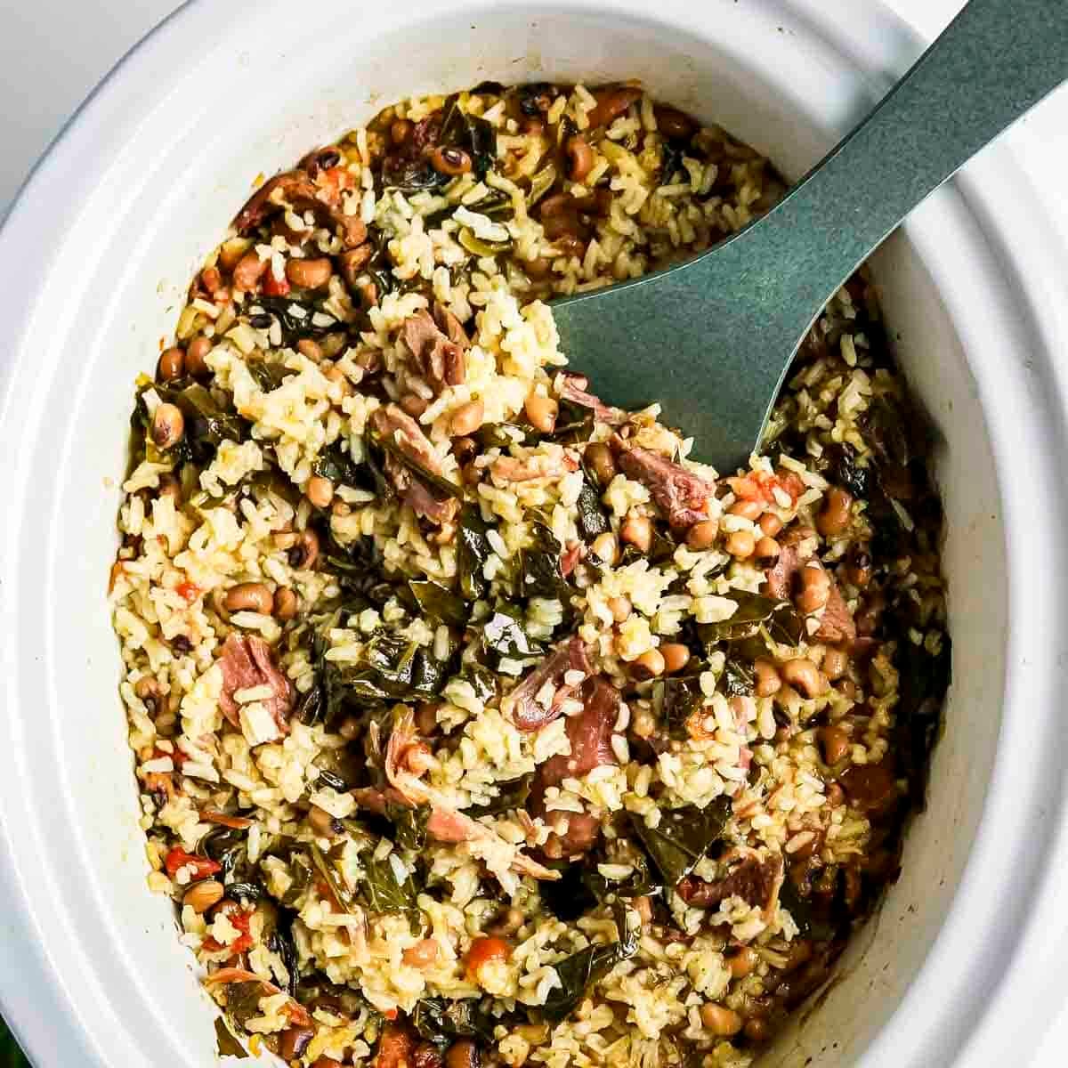 Overhead view of collard greens and peas in a white crock pot bowl with a spoon scooping some out.