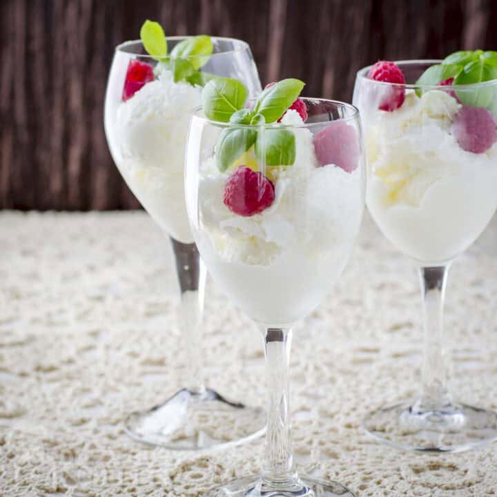 Side shot of three wine glasses with moscato ice cream garnished with raspberries and fresh mint all on a white cloth.