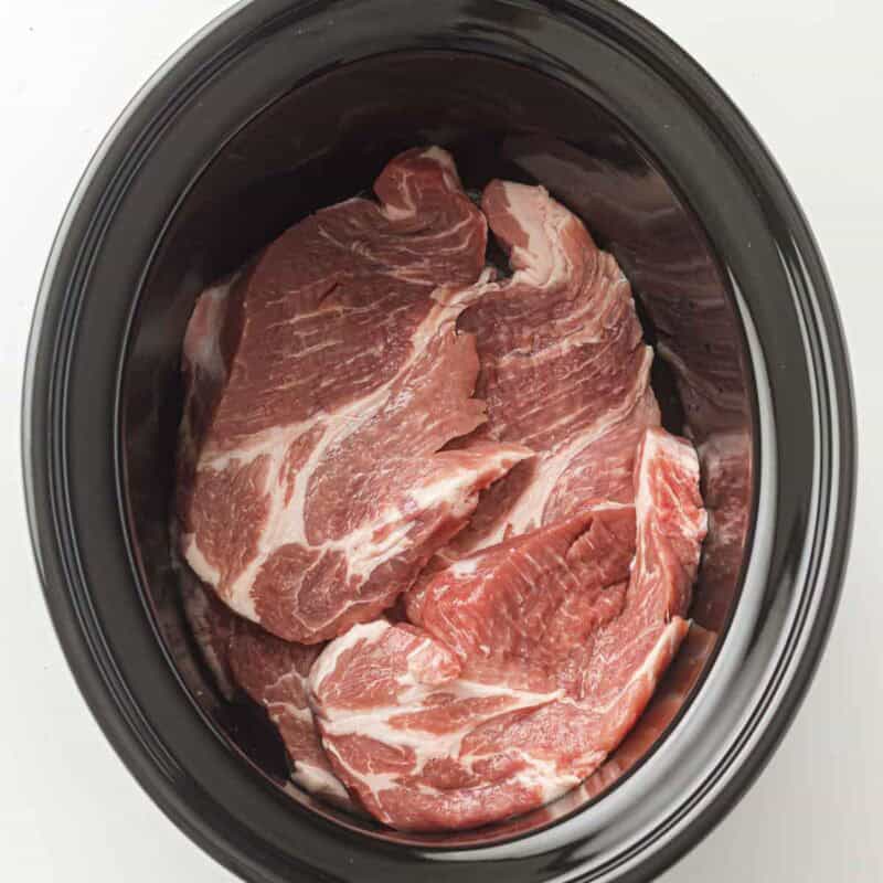 Overhead view of process shot 1 - place the pork shoulder in the slow cooker.