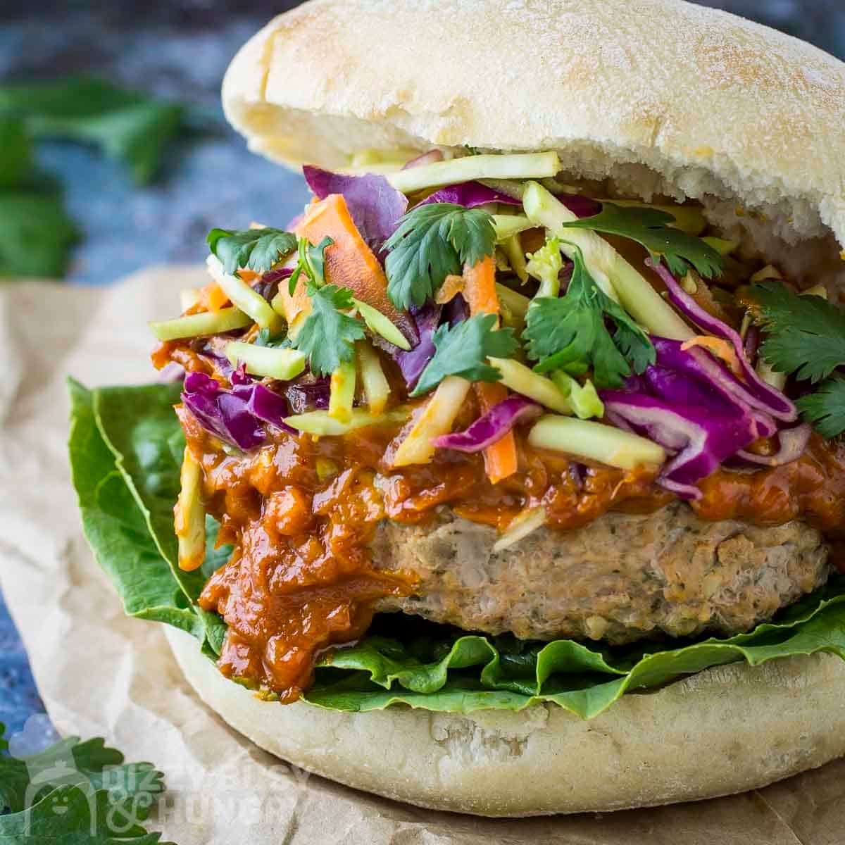 Side close up shot of thai turkey burger garnished with fresh parsley on a piece of brown parchment paper.