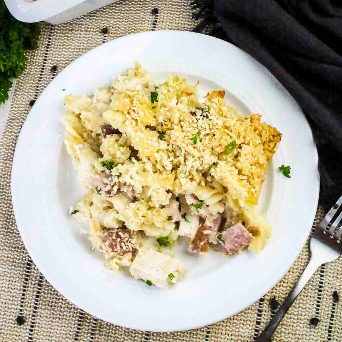 Overhead shot of chicken cordon bleu pasta garnished with fresh herbs on a white plate with a fork on the side.