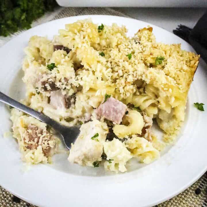 Side shot of chicken cordon bleu pasta garnished with fresh herbs on a white plate with a fork on the side.