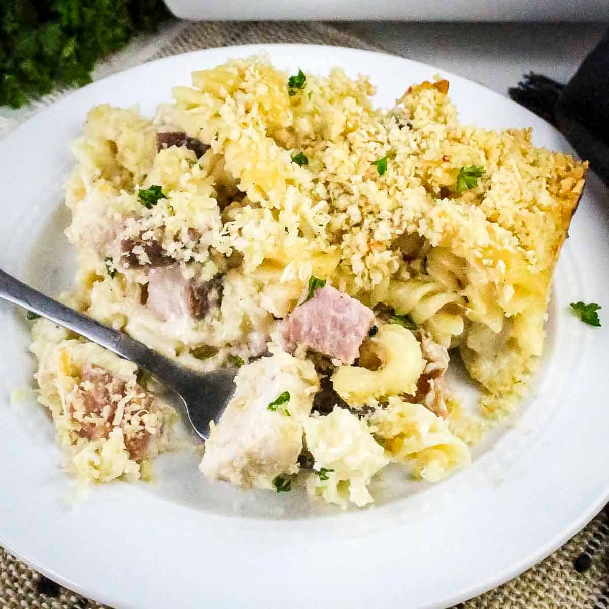 Side shot of chicken cordon bleu pasta garnished with fresh herbs on a white plate with a fork.