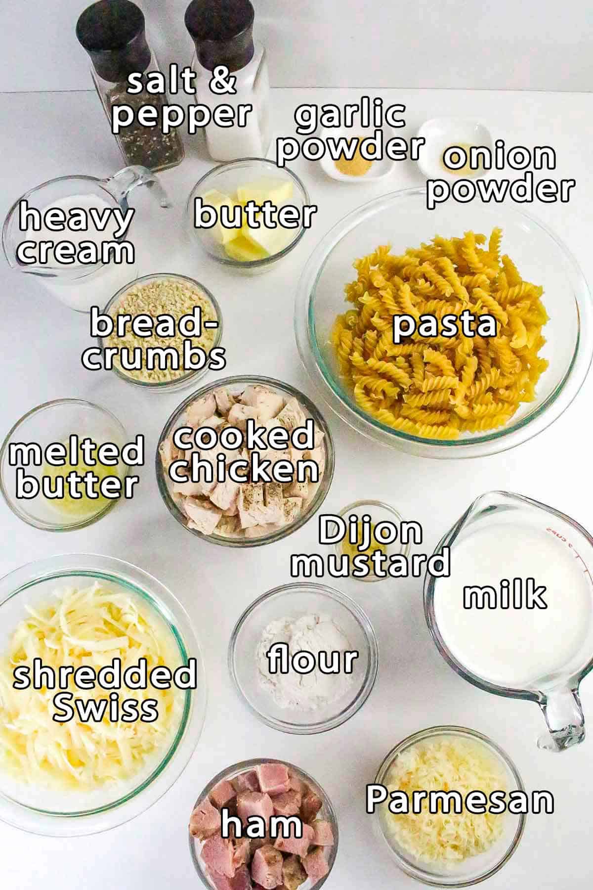 Overhead shot of ingredients - parmesan, ham, milk, flour, shredded swiss, dijon mustard, cooked chicken, pasta, melted butter, breadcrumbs, heavy cream, butter, onion powder, garlic powder, salt, and pepper.