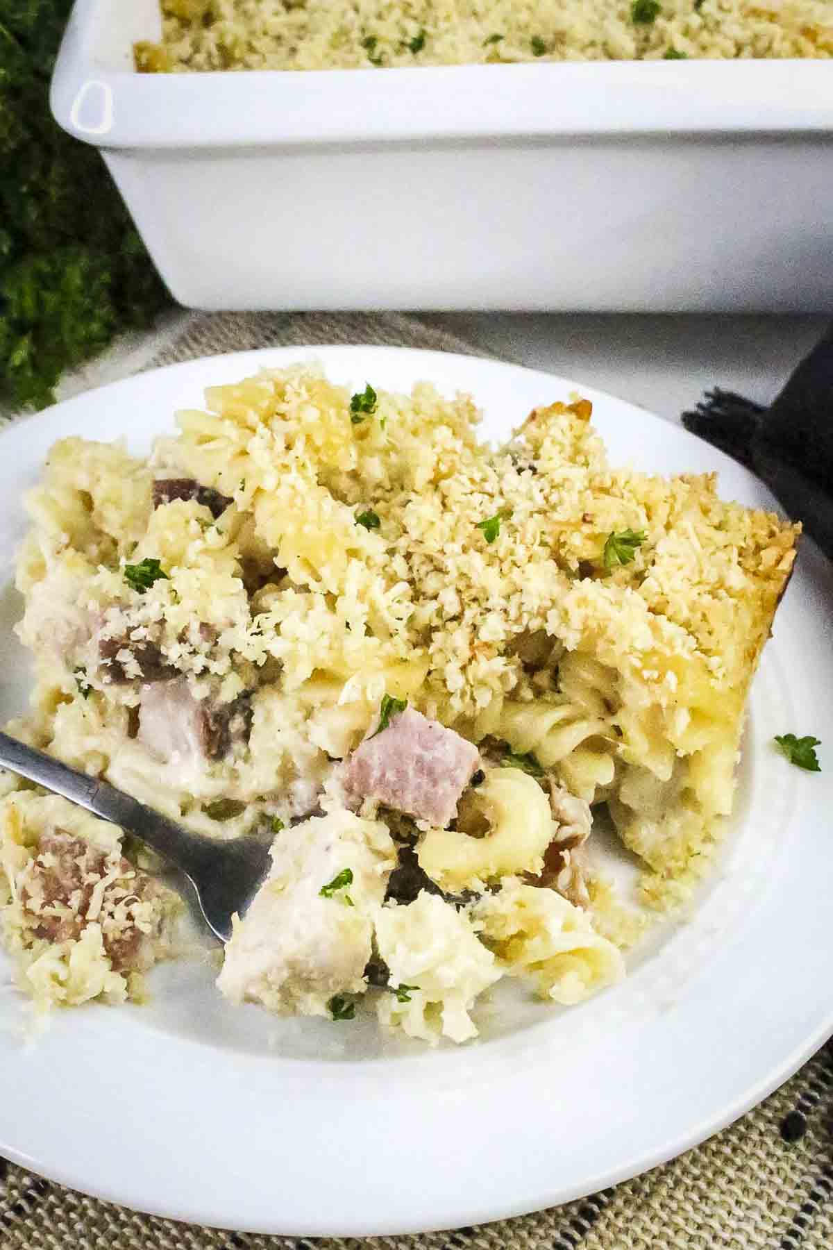 Side shot of chicken cordon bleu pasta garnished with fresh herbs on a white plate with a fork on the side.