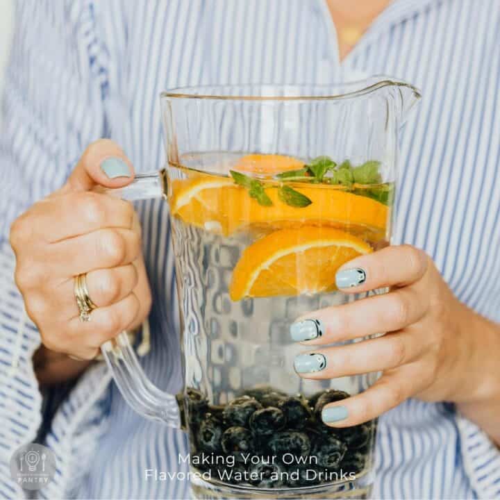 Photo of a person holding a glass pitcher with orange and blueberry flavored water.