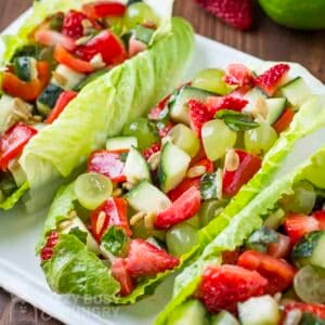 Side close up shot of three lettuce boats filled with fruit and veggie salad on a white plate.