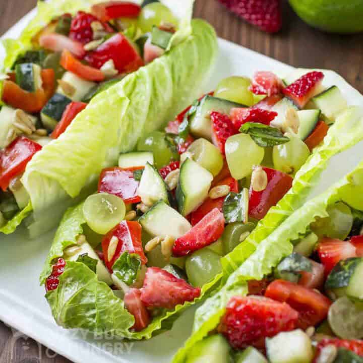 Side close up shot of three lettuce boats filled with fruit and veggie salad on a white plate.